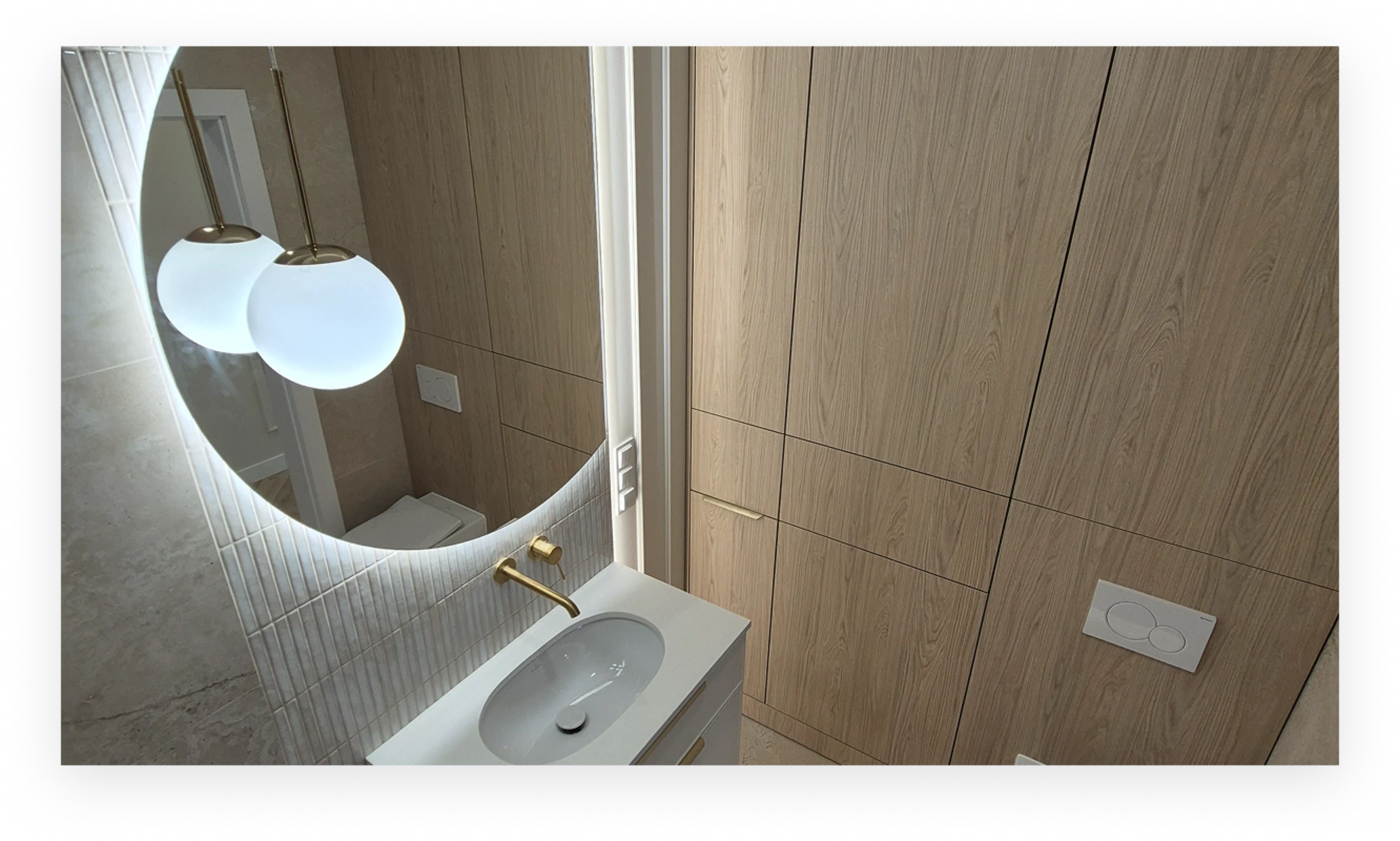 Nowoczesna aranżacja łazienki z podświetlanym lustrem, drewnianą zabudową, złotą baterią i białą umywalką