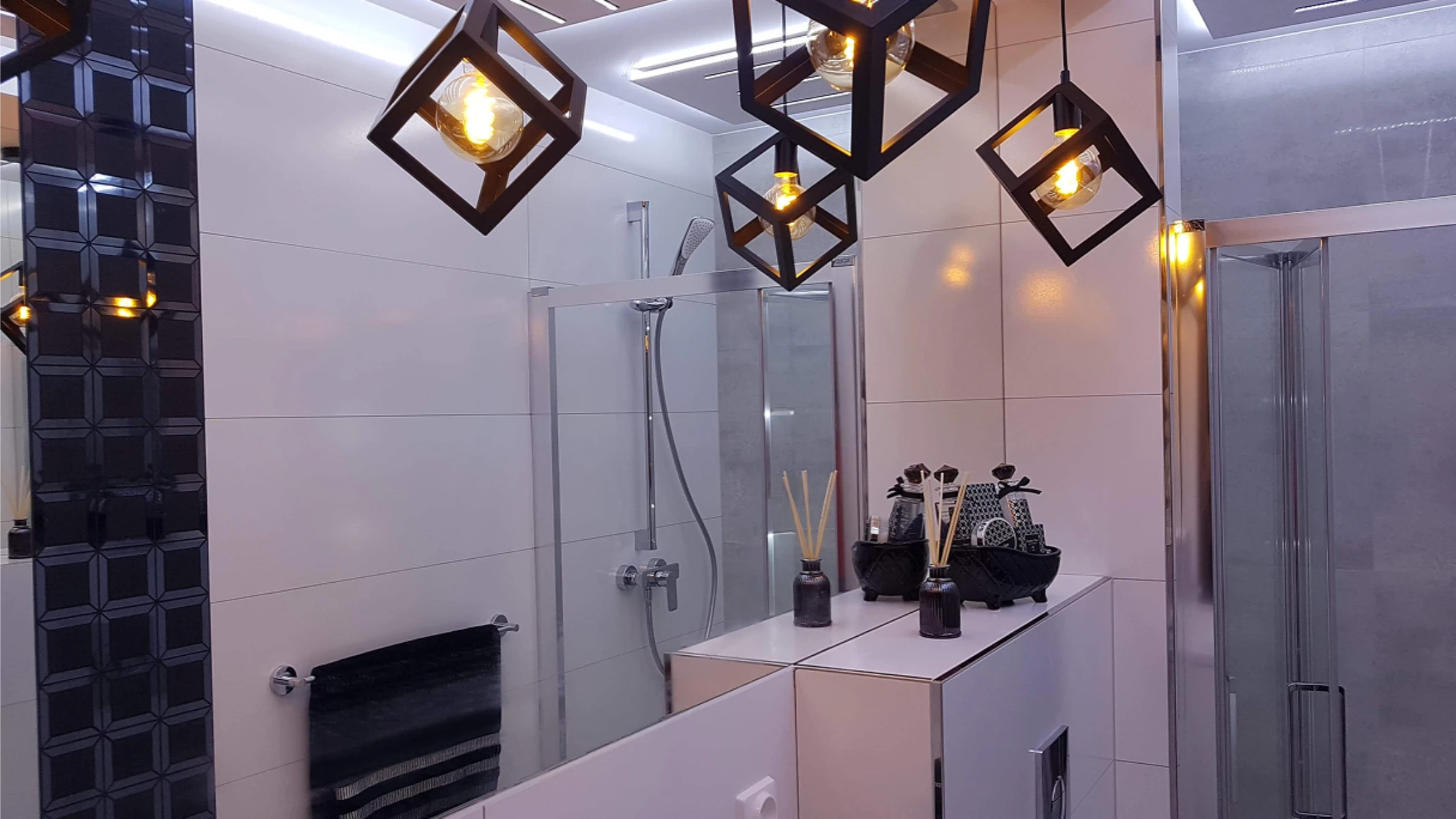 Nowoczesna aranżacja łazienki z białymi płytkami, szklaną kabiną prysznicową i czarnymi akcentami