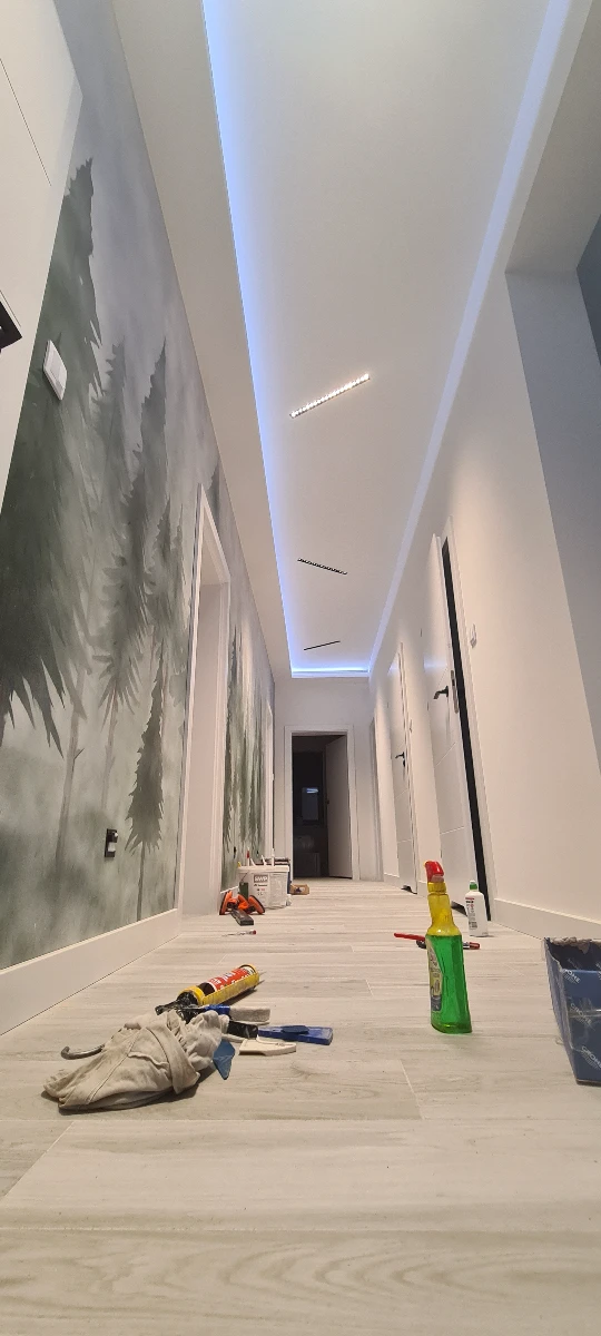 Korytarz z wykonanym sufitem podwieszanym z LED, tapetowaniem ścian motywem lasu i układaniem paneli podłogowych