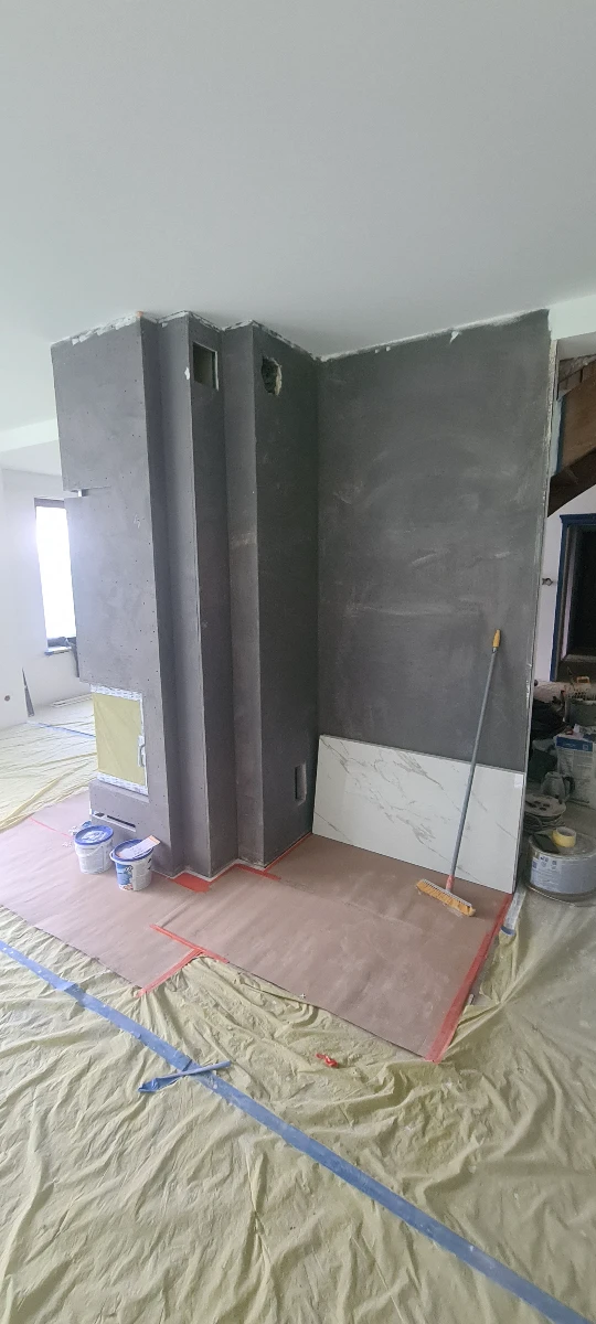 Szara ściana filarowa z nałożoną gładzią, zabezpieczona folią i narzędziami w trakcie wykończenia wnętrza