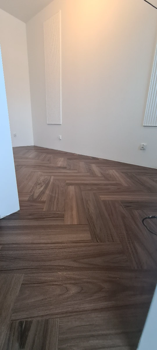 Układanie paneli podłogowych w jodełkę w pustym pokoju z gładkimi białymi ścianami