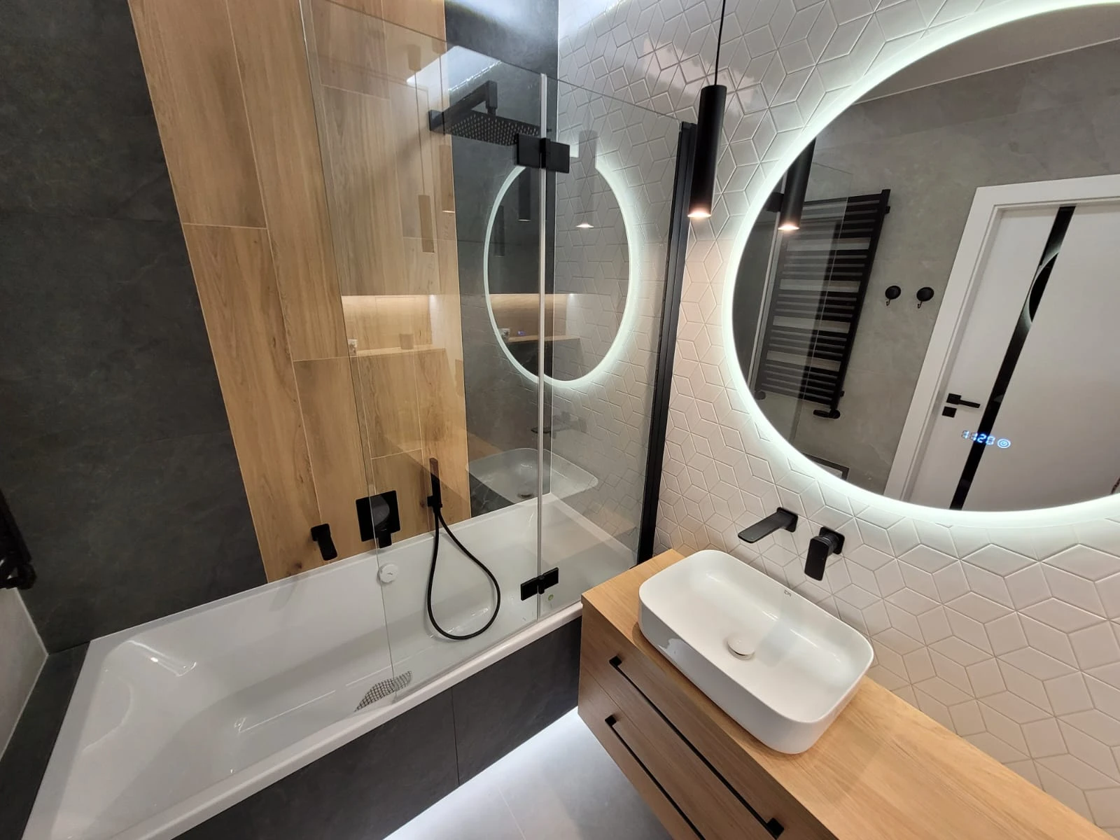 Aranżacja łazienki - nowoczesna przestrzeń z wanną i prysznicem, drewnianą zabudową, czarną armaturą i podświetlanym lustrem