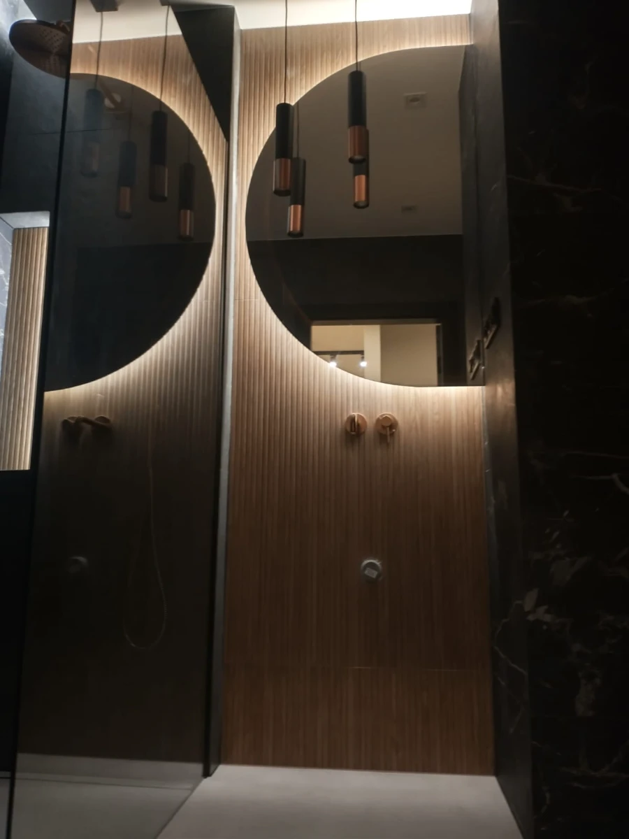 Nowoczesna aranżacja łazienki z drewnianymi panelami ściennymi, dużym okrągłym lustrem i zwieszanymi lampami