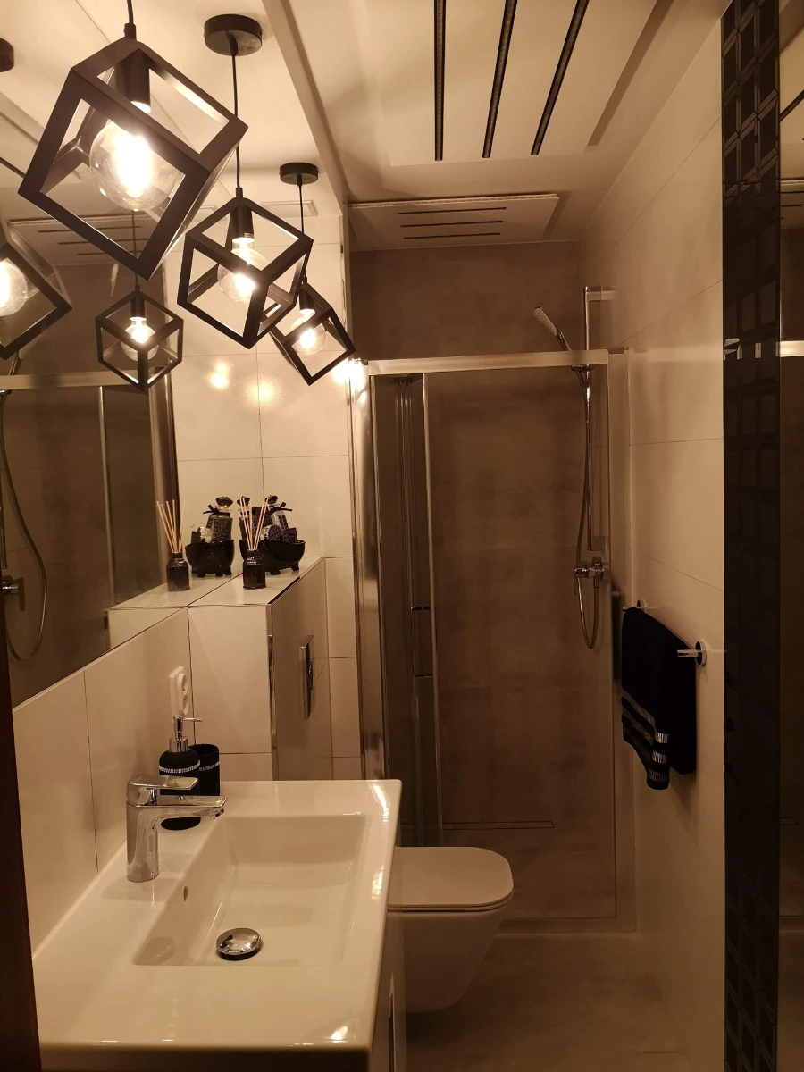 Nowoczesna łazienka z białą umywalką, podwieszaną toaletą, kabiną prysznicową i designerskimi lampami sufitowymi – aranżacja łazienki